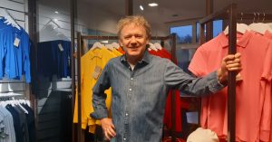 Håkan Pettersson, vd för textilföretaget TG-H och klädmärket Cottover, står framför klädställningar med plagg i olika färger.