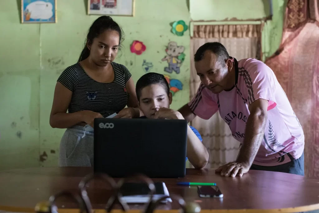 Två ungdomar och en vuxen man som tittar på en datorskärm.